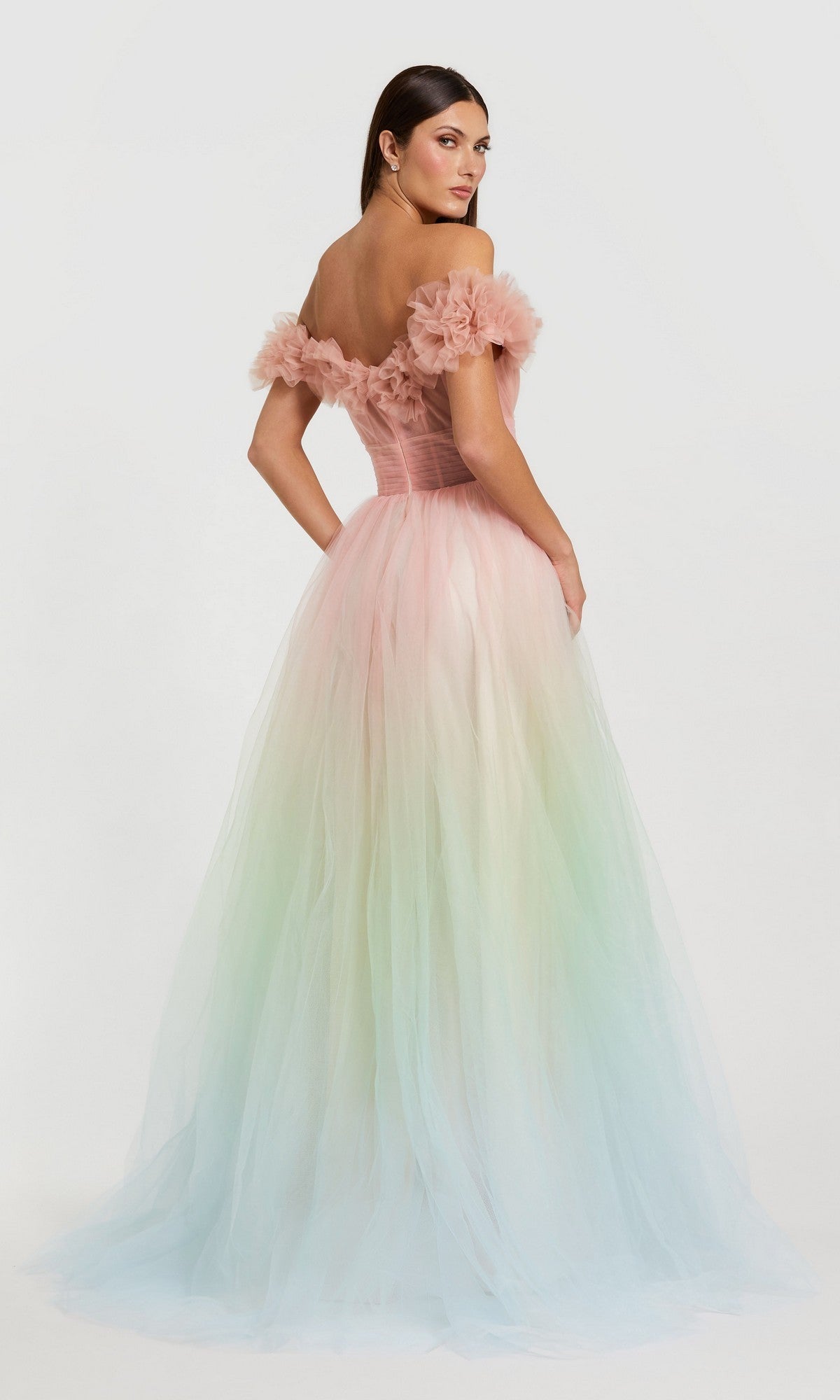 A woman models the Mac Duggal 37002 long prom dress, featuring a fitted off-the-shoulder bodice and a flowing ombre ball gown skirt in pink, green, and blue, posed against a plain white background.